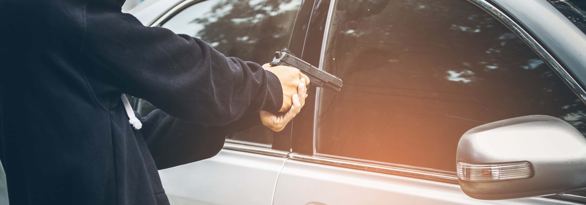 A robber dressed in black pointing a gun at a driver in a car Car thief concept
